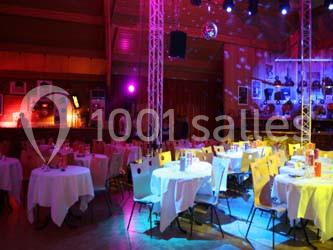 Salle de réception avec tables rondes dressées, éclairage coloré et décorations murales sous des projecteurs.