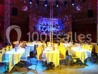 Salle de réception avec des tables rondes dressées, éclairage coloré et écrans suspendus.