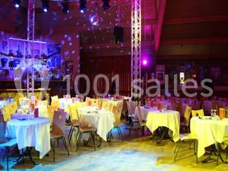 Salle de réception avec des tables rondes dressées, éclairage coloré et écrans suspendus.
