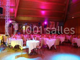 Salle décorée avec des tables rondes dressées, éclairage coloré et ambiance festive.