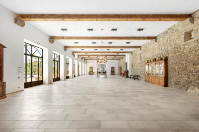 Chambre lumineuse avec lit double, tête de lit rouge, murs en pierre, grandes fenêtres et mobilier classique.