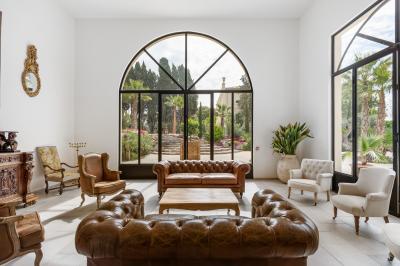 Chambre lumineuse avec lit double, tête de lit rouge, murs en pierre, grandes fenêtres et mobilier classique.