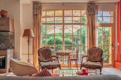 Chambre lumineuse avec lit double, tête de lit rouge, murs en pierre, grandes fenêtres et mobilier classique.