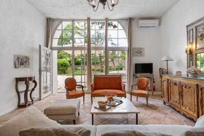 Chambre lumineuse avec lit double, tête de lit rouge, murs en pierre, grandes fenêtres et mobilier classique.