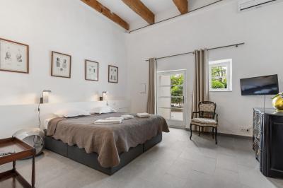 Chambre lumineuse avec lit double, tête de lit rouge, murs en pierre, grandes fenêtres et mobilier classique.