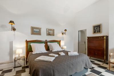 Chambre lumineuse avec lit double, tête de lit rouge, murs en pierre, grandes fenêtres et mobilier classique.