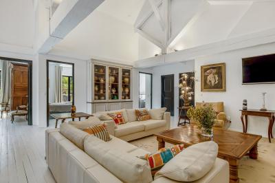 Chambre lumineuse avec lit double, tête de lit rouge, murs en pierre, grandes fenêtres et mobilier classique.