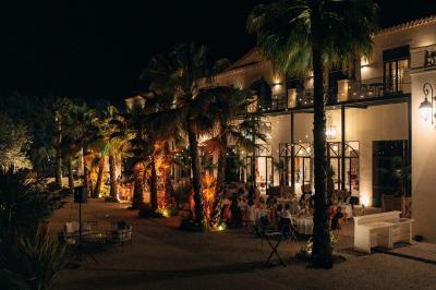 Chambre lumineuse avec lit double, tête de lit rouge, murs en pierre, grandes fenêtres et mobilier classique.