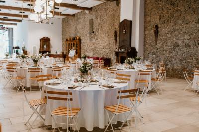 Chambre lumineuse avec lit double, tête de lit rouge, murs en pierre, grandes fenêtres et mobilier classique.