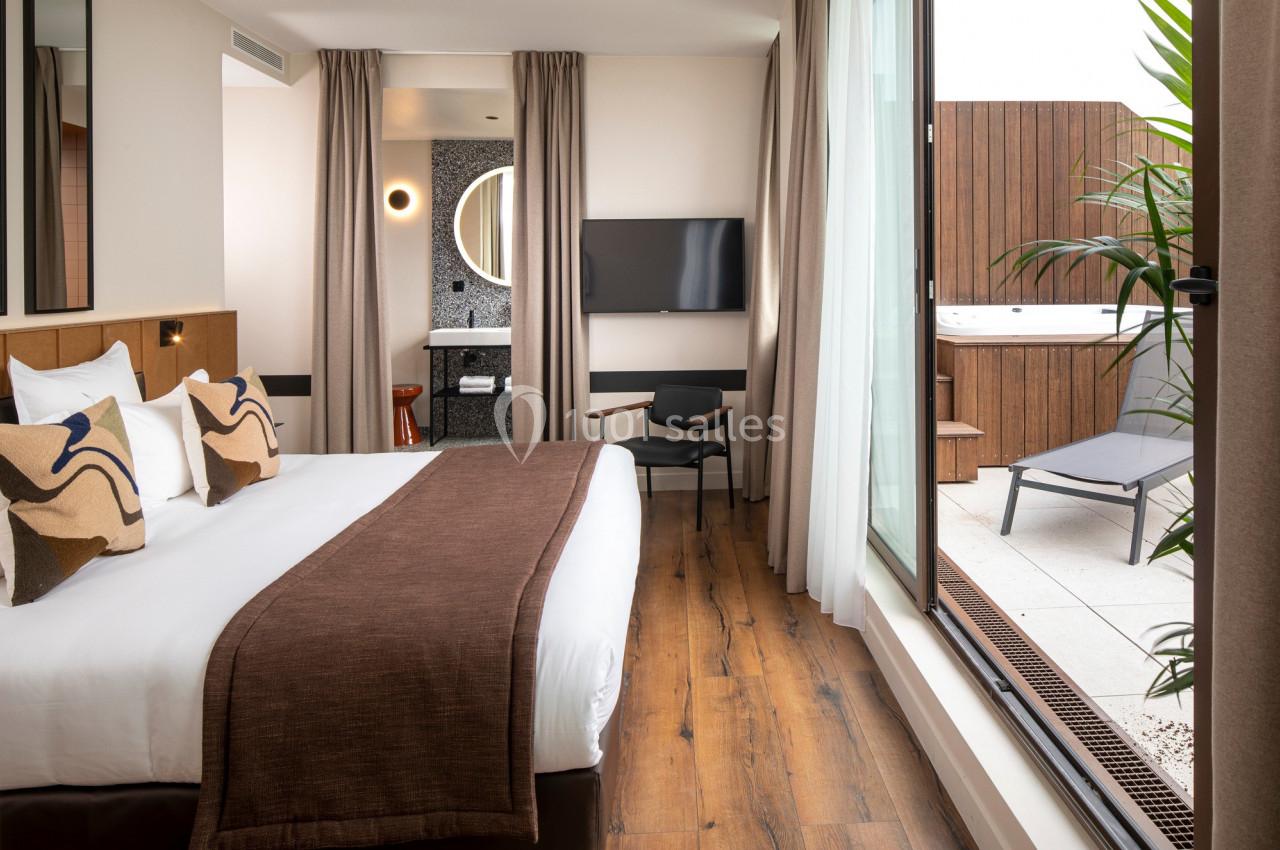 Chambre d'hôtel moderne avec lit double, télévision, fauteuil, terrasse extérieure et bain à remous.
