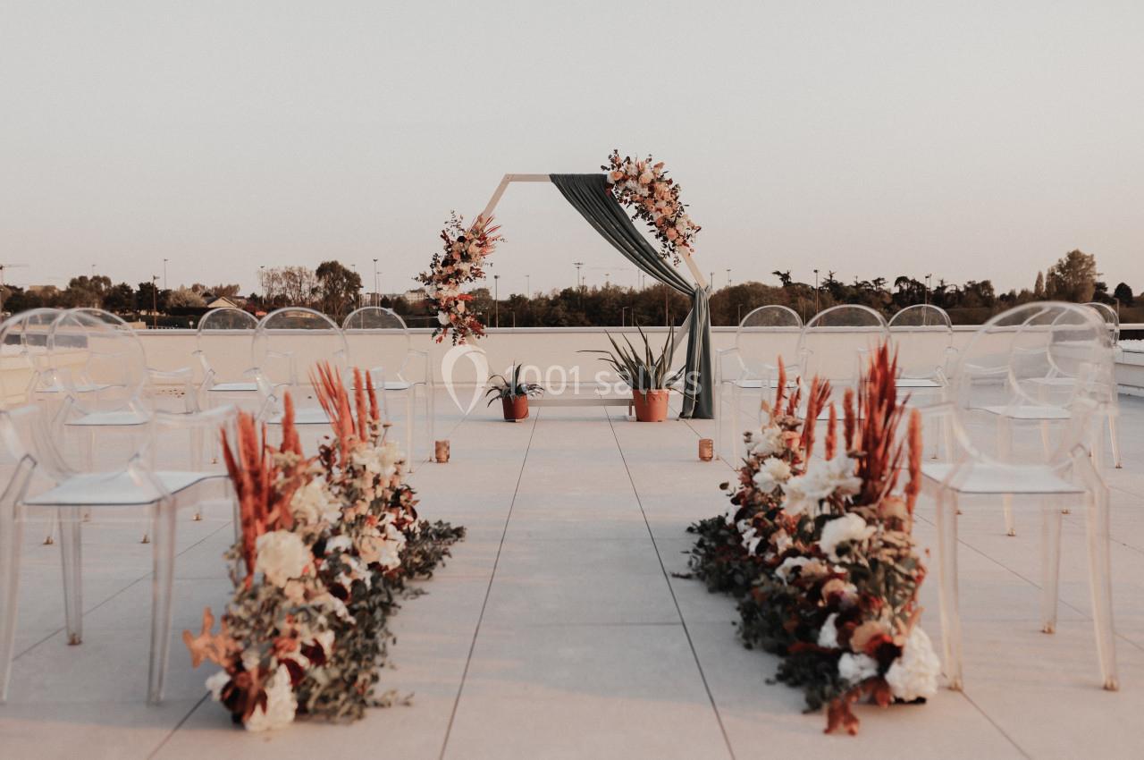 Allée décorée de fleurs menant à une arche ornée de feuillages et fleurs, installée sur une terrasse extérieure.