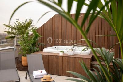 Bain à remous entouré de plantes et de transats sur une terrasse en bois avec vue dégagée.