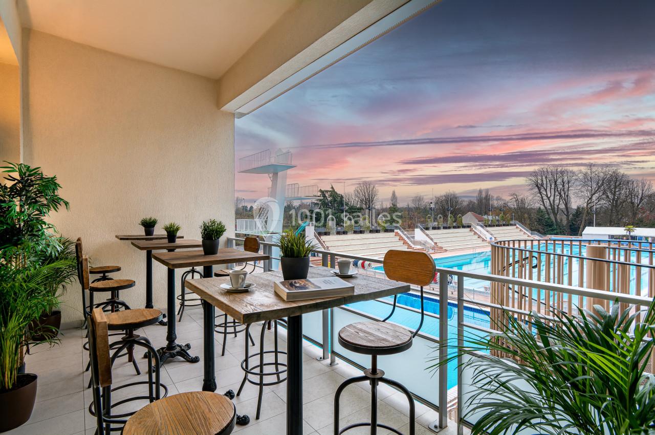 Terrasse aménagée avec tables et plantes, offrant une vue sur une piscine extérieure et un ciel au coucher du soleil.