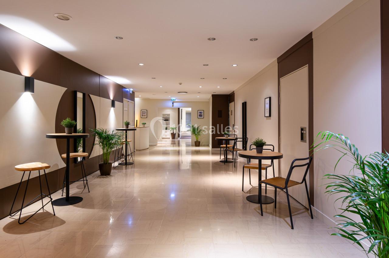 Espace intérieur lumineux avec tables hautes, chaises, plantes décoratives et sol en carrelage clair.