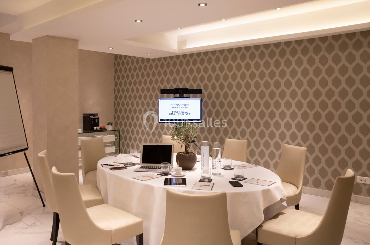 Salle de réunion avec table ronde, chaises, écran mural, bloc-notes, ordinateur portable et machine à café en arrière-plan.