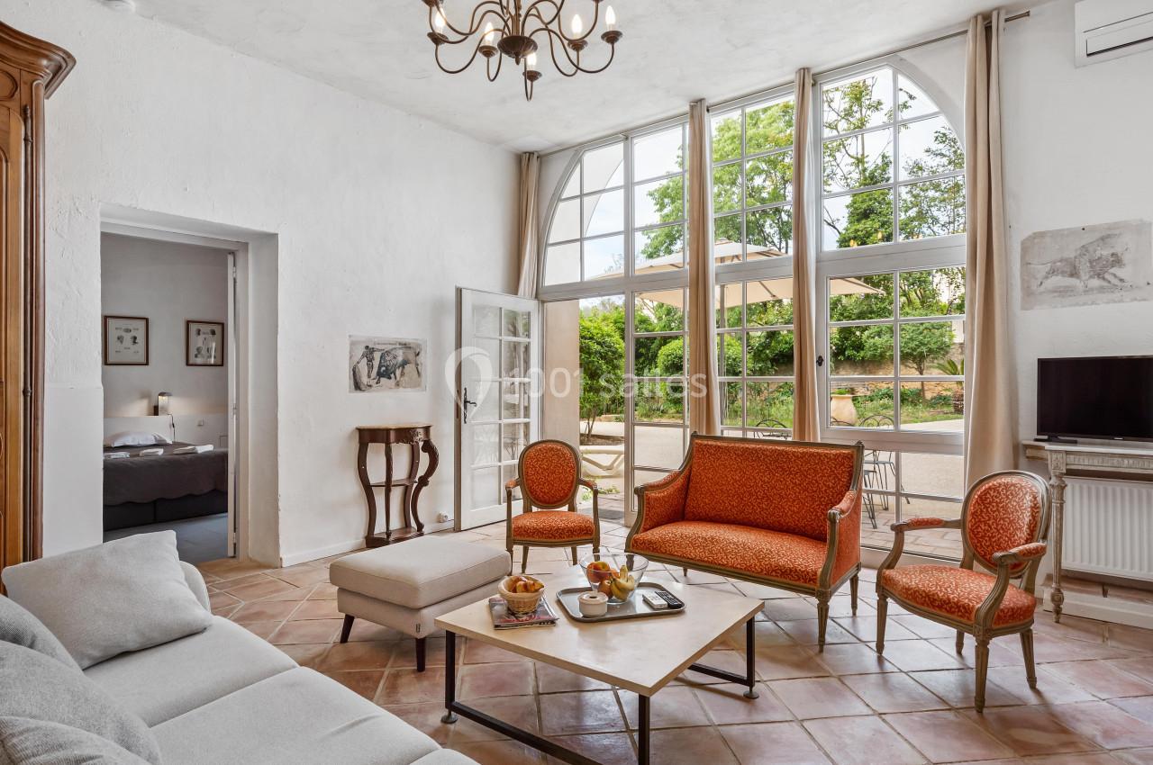 Salon lumineux avec grandes fenêtres, mobilier ancien, canapé, fauteuils orange et table basse avec collations.