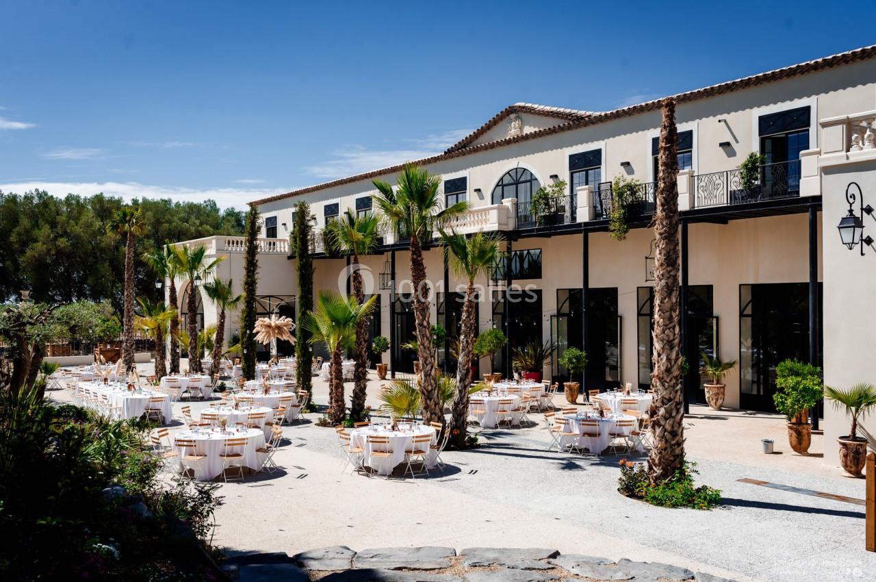 Terrasse d'un bâtiment élégant avec des tables dressées pour un événement, entourée de palmiers et de végétation.