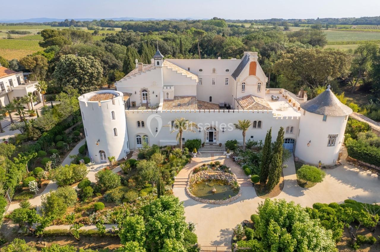 Vue aérienne d'un château blanc entouré de jardins verdoyants et de paysages champêtres.