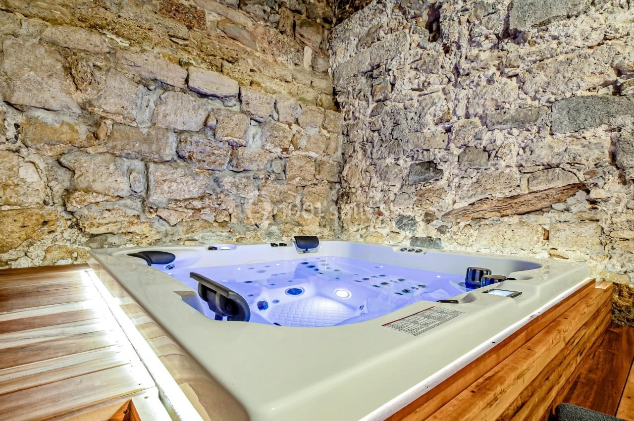 Jacuzzi encastré dans un espace intérieur avec murs en pierre apparente et éclairage doux.