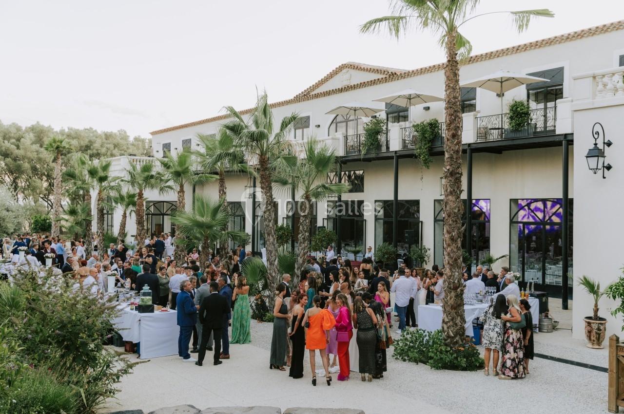 Groupe de personnes rassemblées lors d'un événement en plein air devant un bâtiment blanc entouré de palmiers.