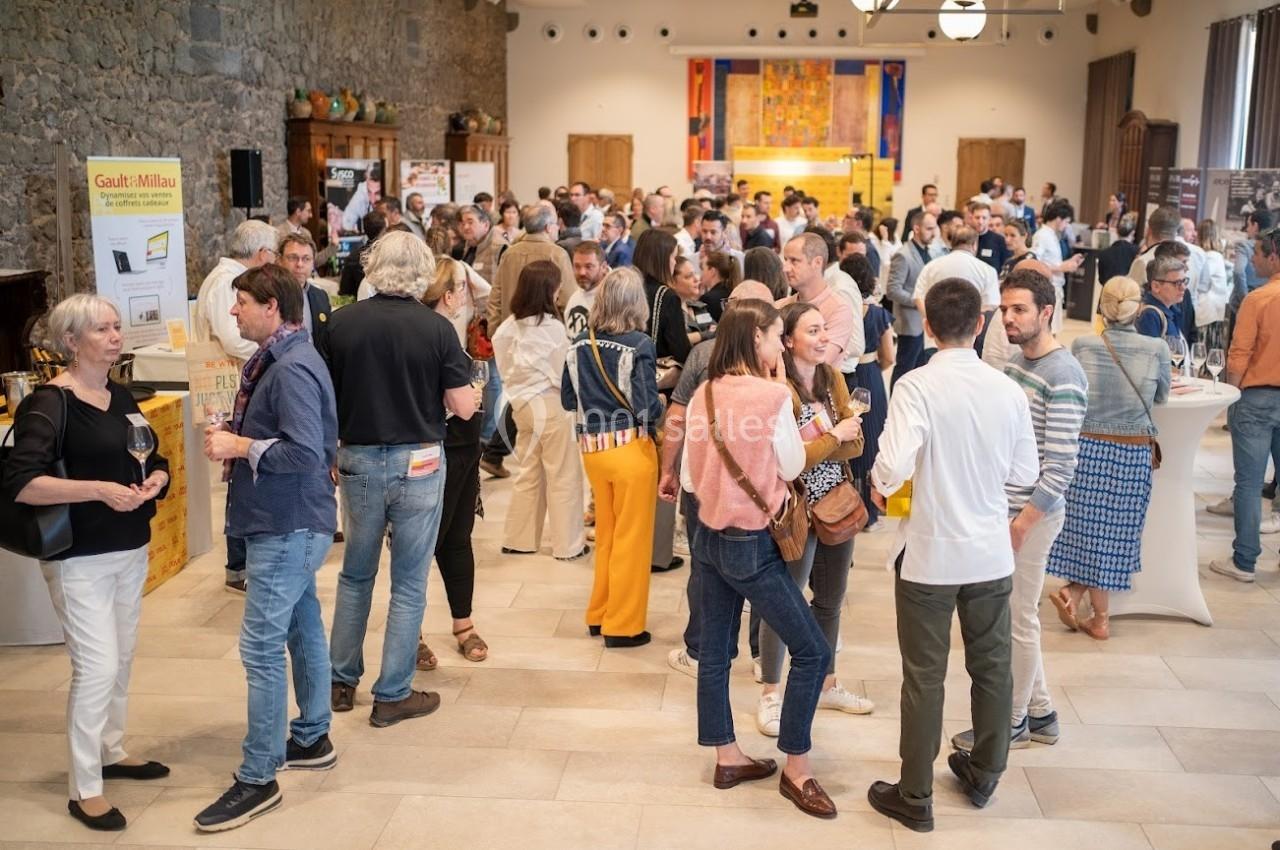 Groupe de personnes échangeant et dégustant du vin dans une salle lumineuse avec des stands et une ambiance conviviale.