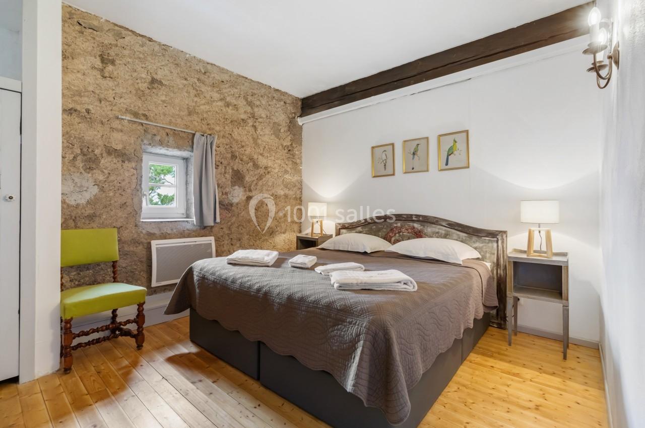 Chambre avec un lit double, murs en pierre et bois, deux lampes de chevet, une chaise et une petite fenêtre.