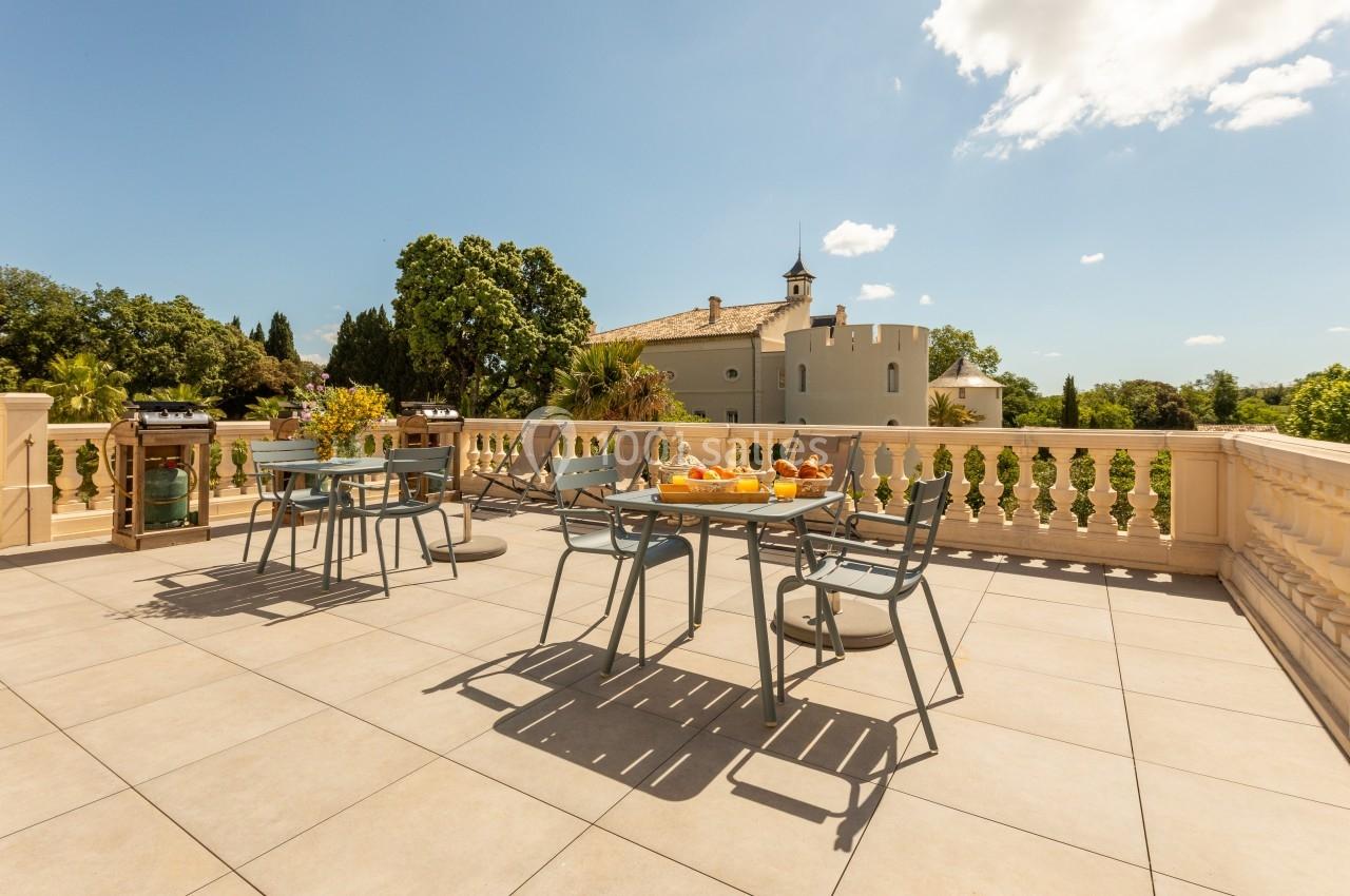 Terrasse ensoleillée avec tables et chaises, vue sur un bâtiment de style château entouré de verdure.