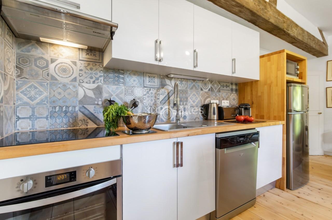 Cuisine moderne avec plan de travail en bois, crédence en carreaux décoratifs, électroménagers inox et rangements blancs.