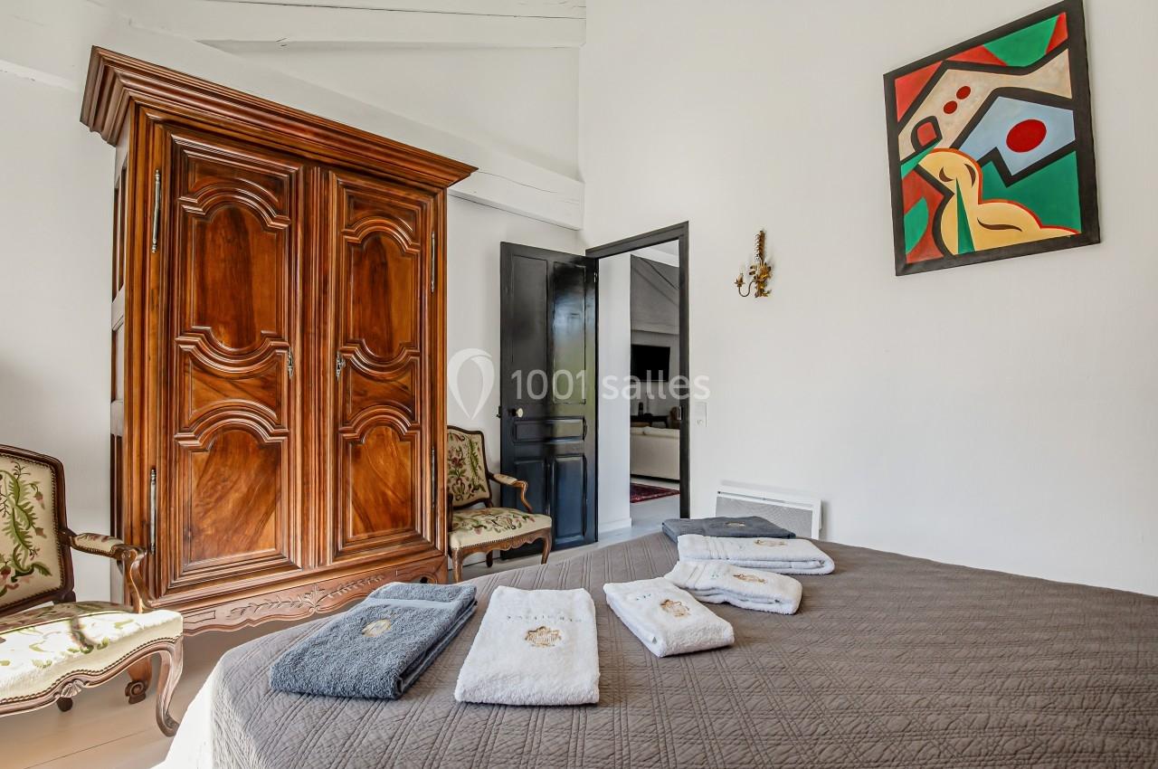 Chambre avec armoire en bois, lit recouvert d'une couverture marron et serviettes pliées, décorée d'un tableau coloré.