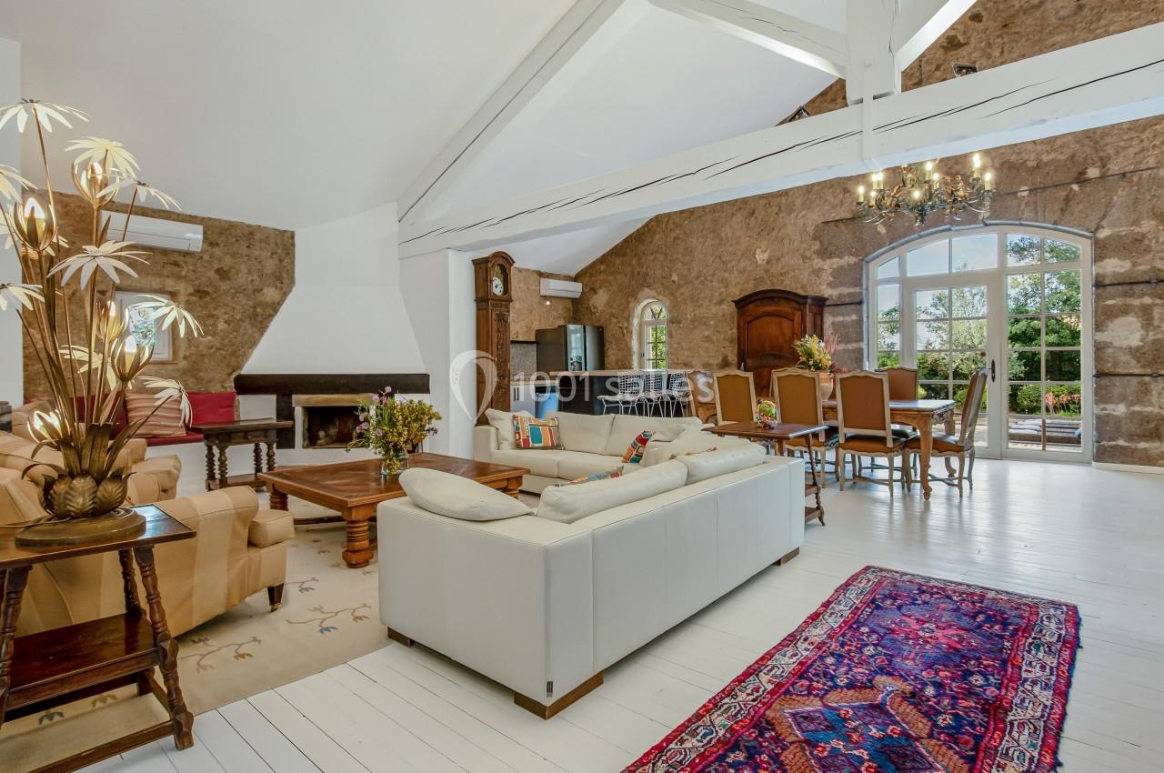 Salon spacieux avec poutres apparentes, mobilier élégant, cheminée, tapis coloré et vue sur jardin par une grande baie…