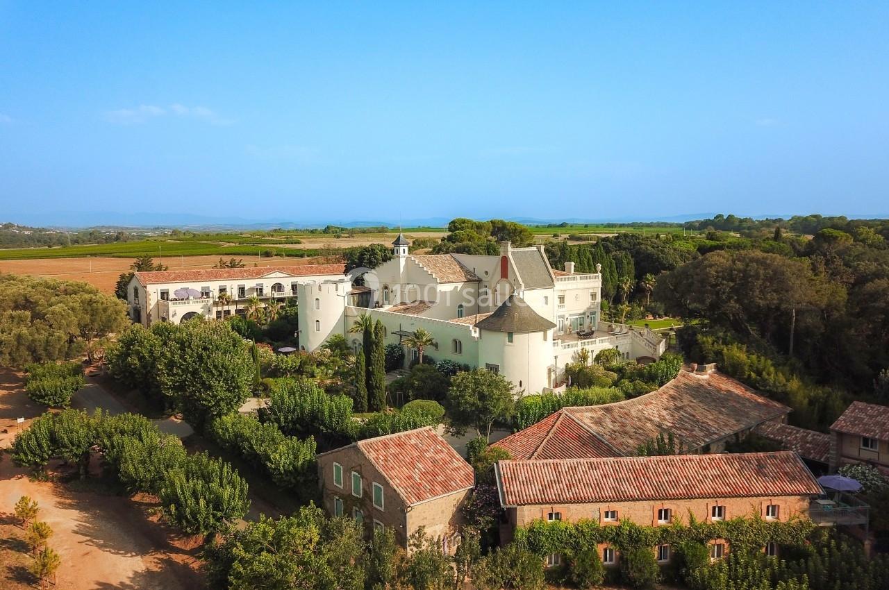 Vue aérienne d'un domaine avec bâtiments en pierre, toits en tuiles, jardins verdoyants et paysage rural en arrière-plan.
