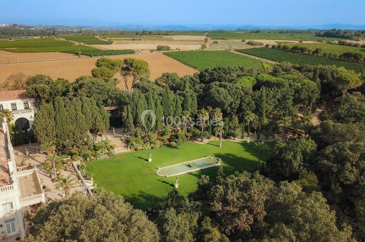 Vue aérienne d'un jardin avec pelouse, bassin central, arbres et paysage de campagne en arrière-plan.
