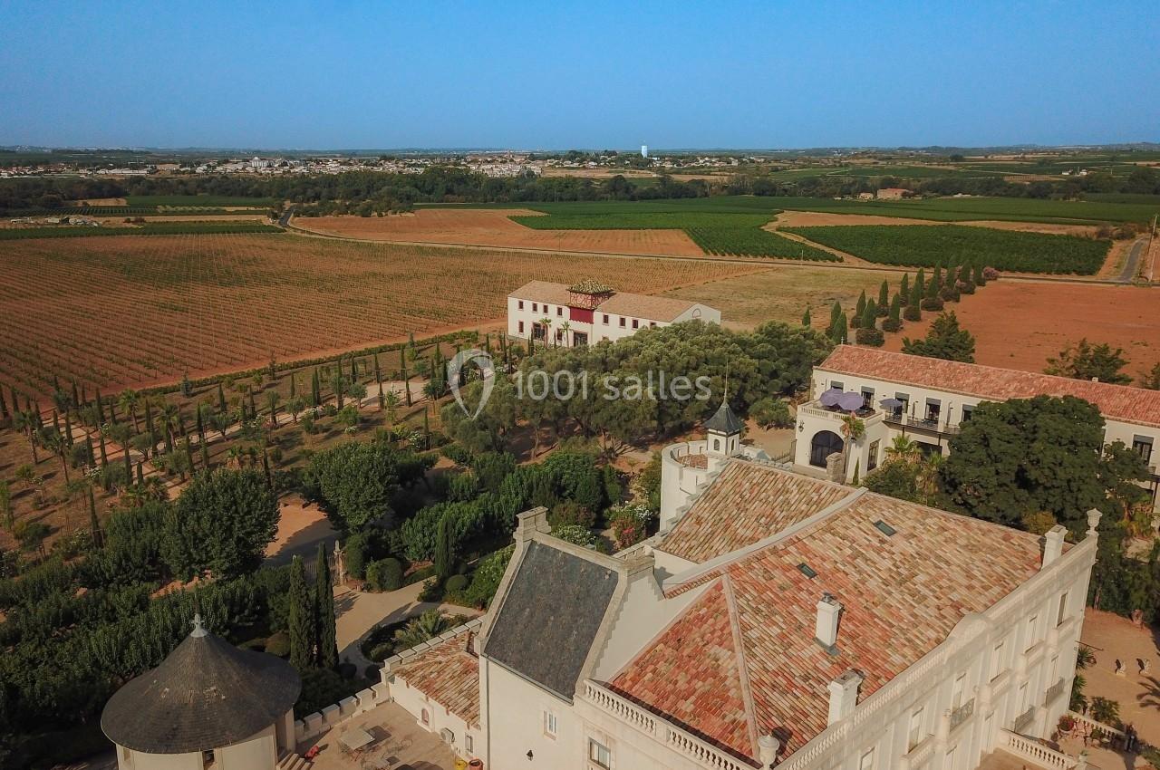 Vue aérienne d'un domaine viticole avec bâtiments anciens, vignes et paysage rural sous un ciel dégagé.