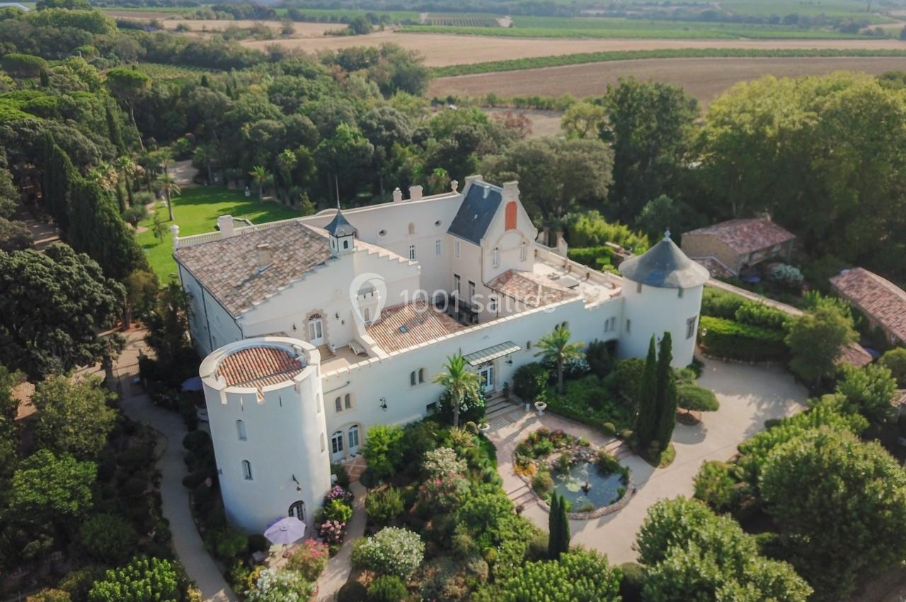 Vue aérienne d'un château blanc entouré de jardins verdoyants et de paysages agricoles.