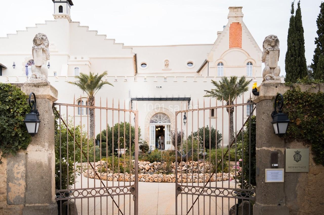Façade d'un bâtiment historique avec portail en fer forgé, statues de lions et jardin paysager à l'entrée.