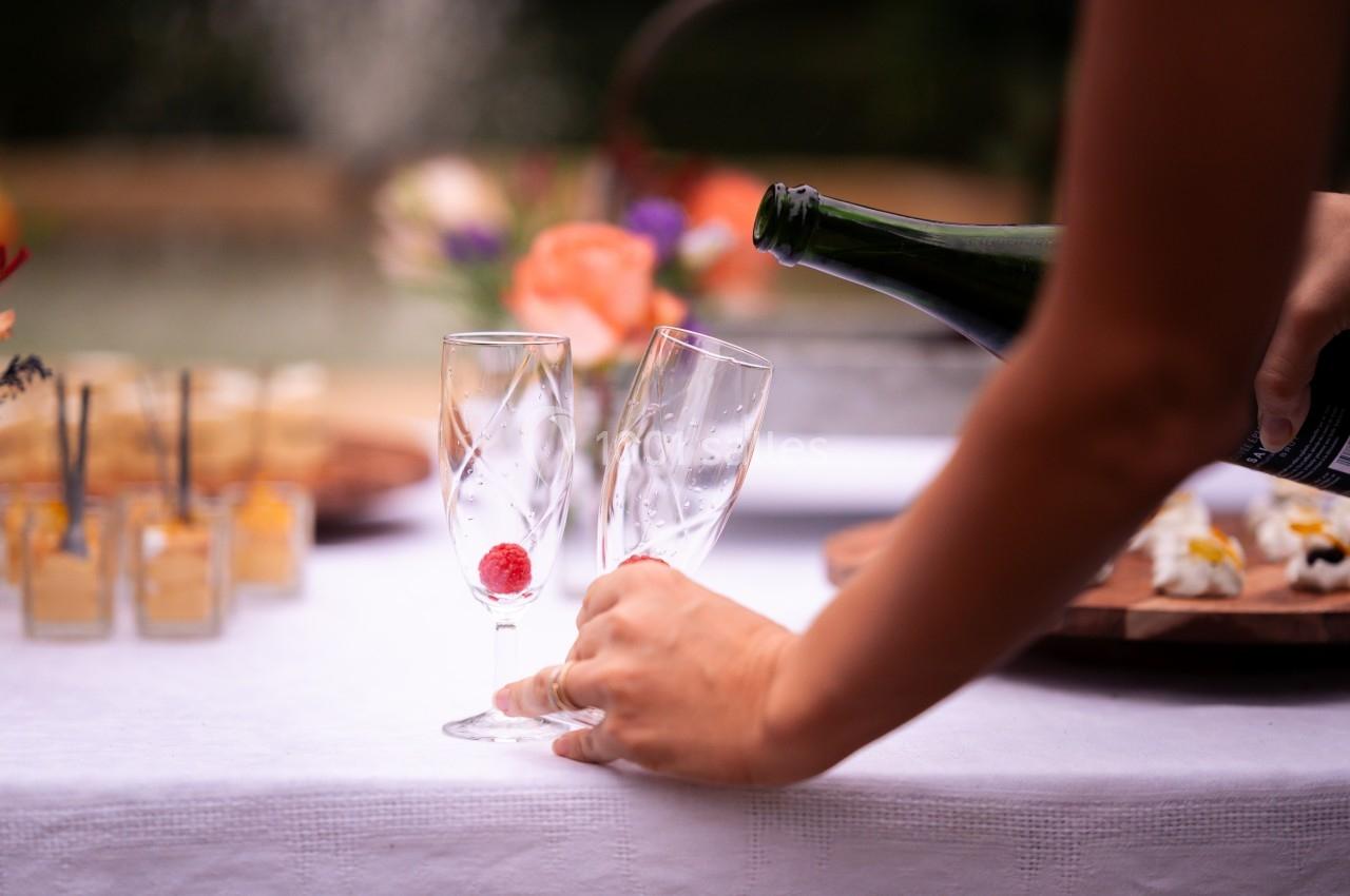 Une main verse du champagne dans deux flûtes sur une table dressée avec des amuse-bouches en arrière-plan.