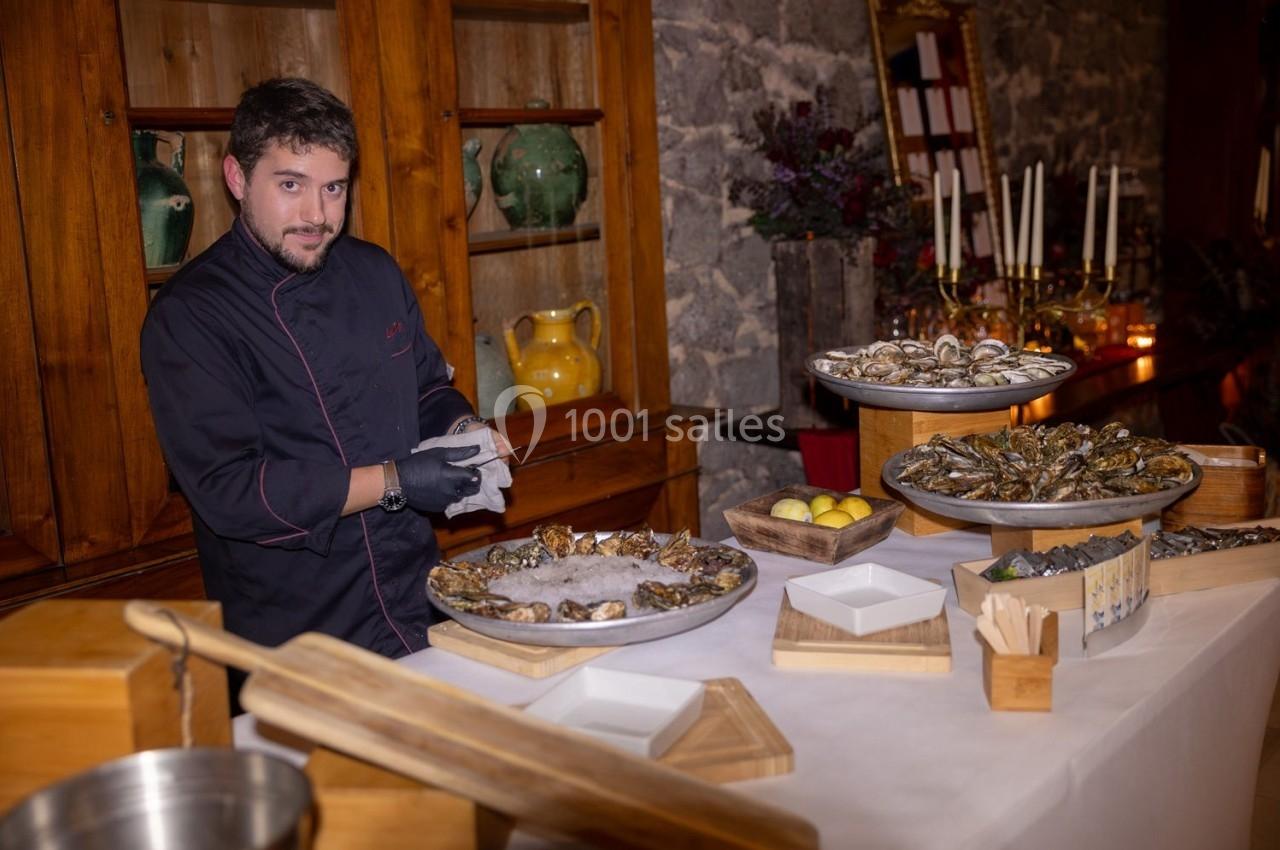 Un chef prépare des huîtres sur un stand avec des plateaux garnis, dans un cadre rustique avec des bougies et des…