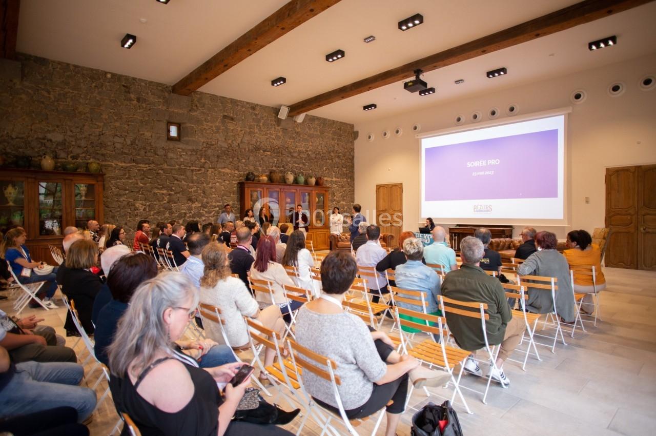 Personnes assises dans une salle de conférence avec un écran projetant une présentation devant un mur en pierre.