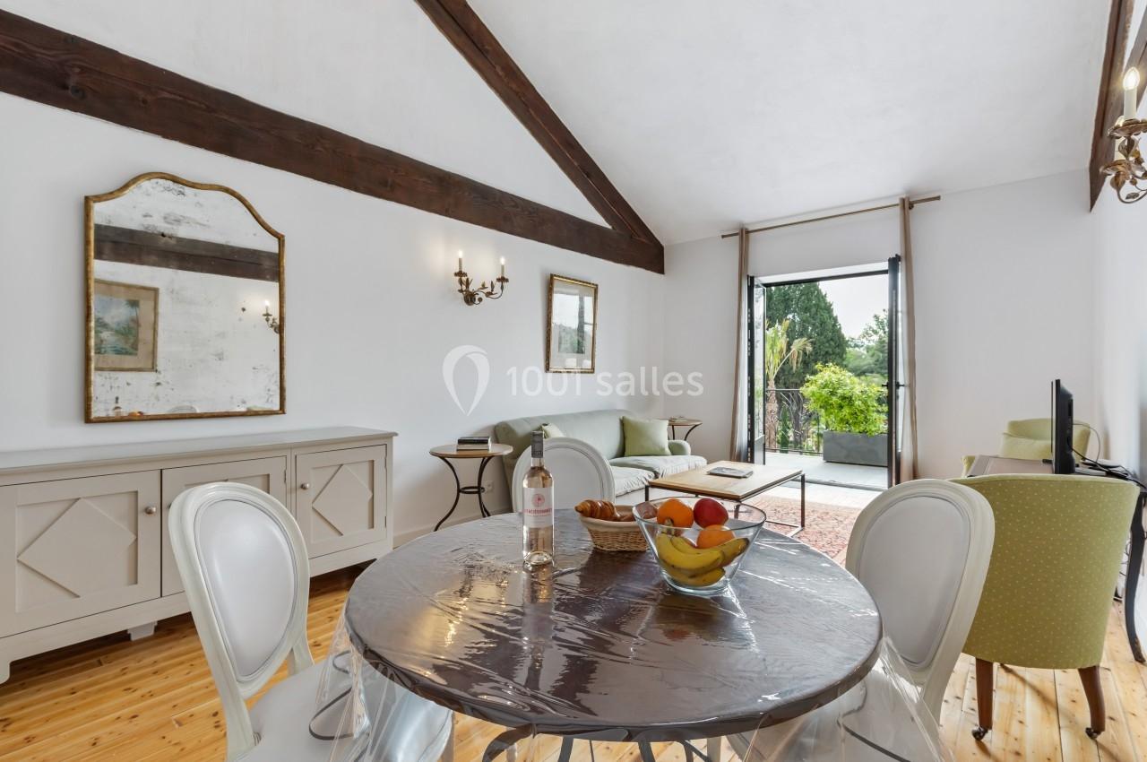Salle de séjour lumineuse avec table à manger, canapé, miroir mural, et vue sur un jardin depuis une porte vitrée.