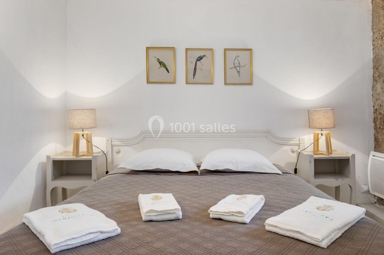 Lit double avec couvre-lit marron, serviettes pliées au premier plan, deux lampes de chevet et trois cadres muraux.