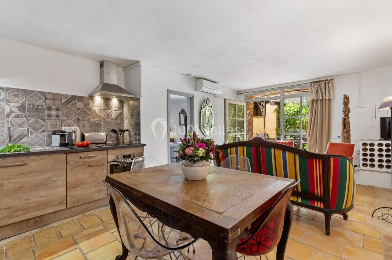 Cuisine ouverte avec plan de travail en bois, carrelage décoratif, table en bois et salon coloré donnant sur un jardin.