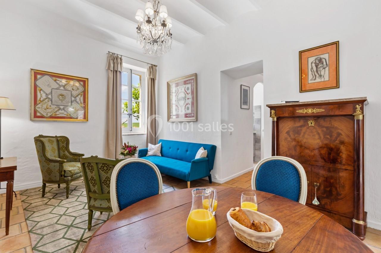 Salon lumineux avec mobilier classique, canapé bleu, table en bois, chaises rembourrées et carafe de jus d'orange.
