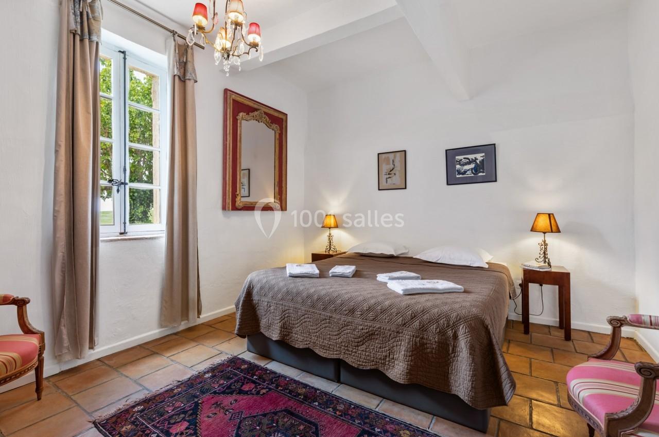 Chambre lumineuse avec un lit double, des lampes de chevet, un tapis coloré et une fenêtre donnant sur un espace vert.