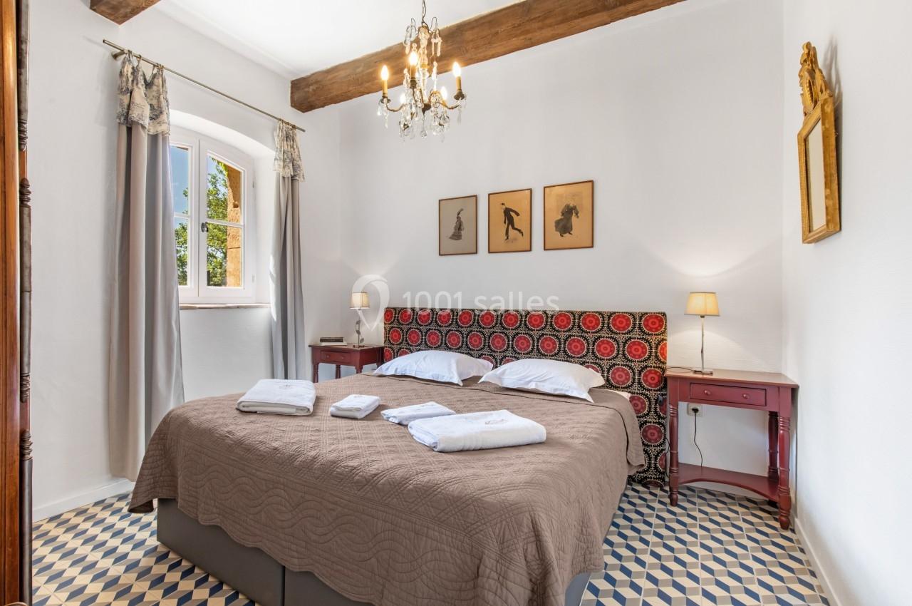 Chambre lumineuse avec lit double, couvre-lit marron, tables de chevet rouges, lustre et fenêtre donnant sur l'extérieur.