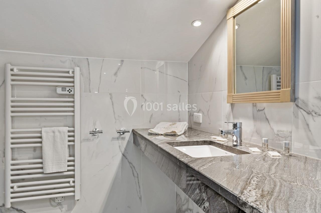 Salle de bain avec lavabo en marbre, miroir encadré, porte-serviettes chauffant et murs en carrelage effet marbre.