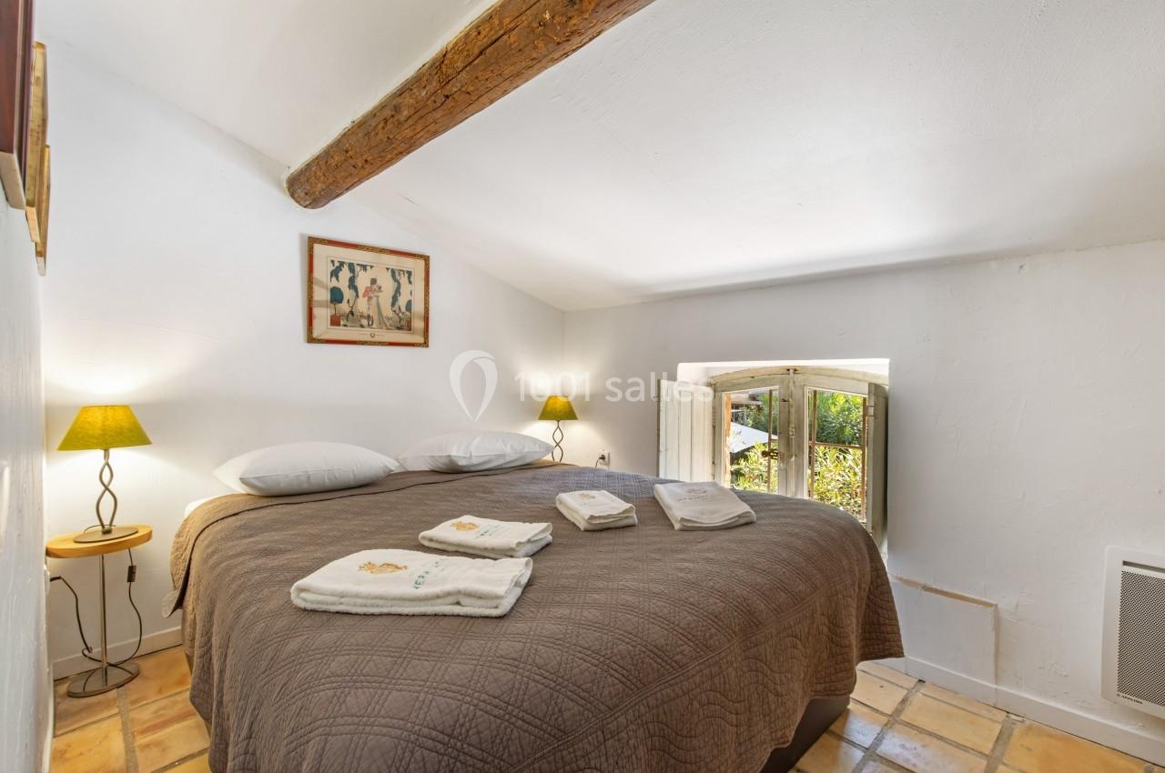 Chambre lumineuse avec lit double, poutre apparente, lampes de chevet et fenêtre donnant sur un jardin.