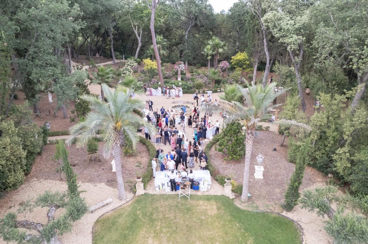 Vue aérienne d'un rassemblement en plein air dans un jardin arboré avec des tables et des invités.