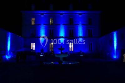 Façade d'un bâtiment éclairé en bleu la nuit, avec une fontaine au premier plan.