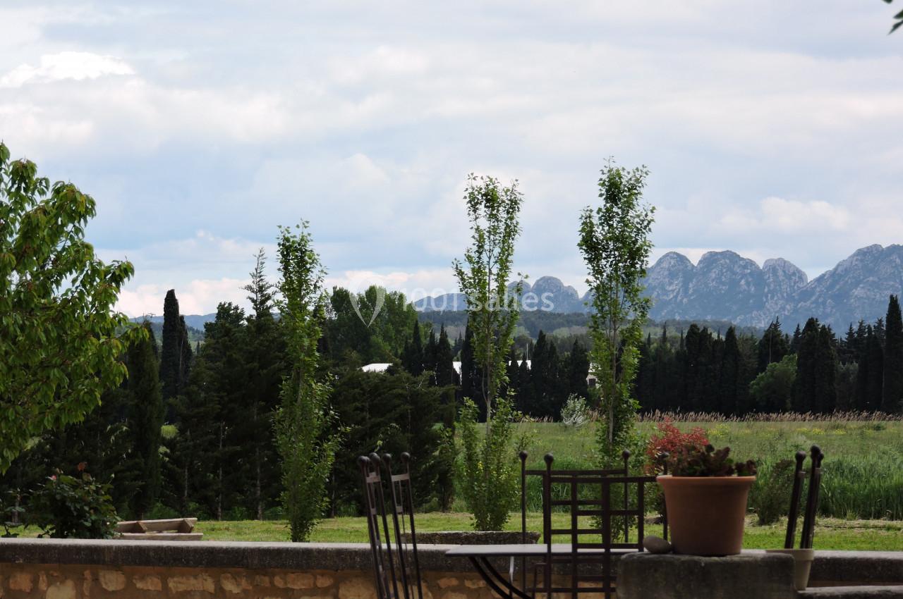 Paysage rural avec des arbres, des montagnes en arrière-plan et une terrasse en pierre avec des chaises et une plante en pot.