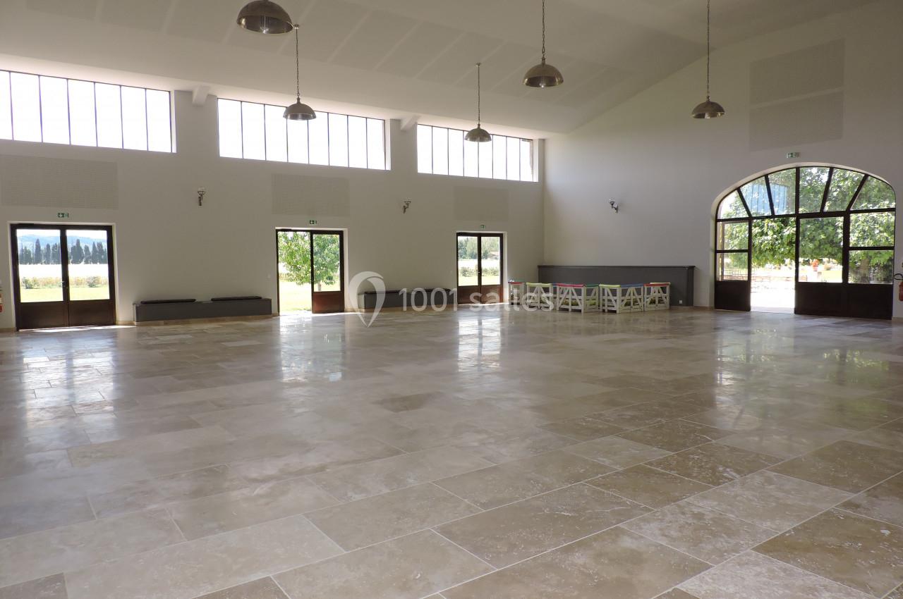 Salle spacieuse et lumineuse avec un sol en pierre, de grandes fenêtres et des portes donnant sur un espace extérieur…